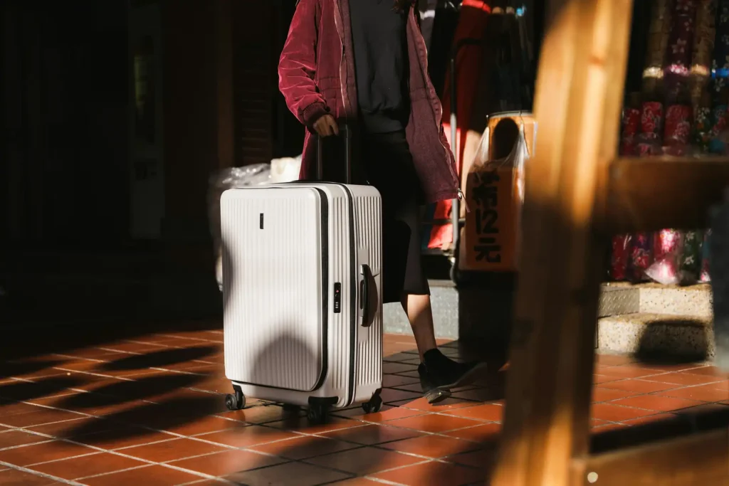 Photo of a person from the shoulders down walking with a white suitcase