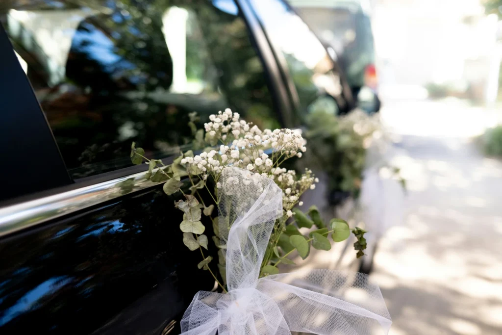 Image of a black van, with a posy of wedding flowers attached to the door on its way to the service