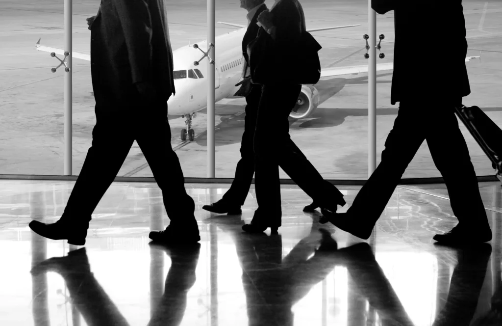 4 men in suits walking through an airport terminal in front of a window looking out onto the runway.